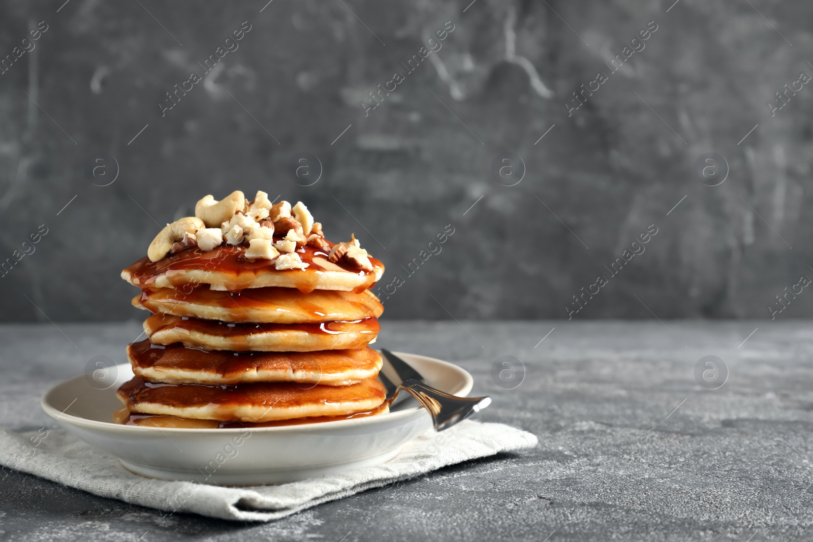 Photo of Stack of tasty pancakes with nuts and syrup on table