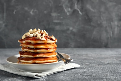 Photo of Stack of tasty pancakes with nuts and syrup on table