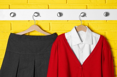 Photo of Shirt, jumper and skirt hanging on yellow brick wall. School uniform