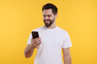 Photo of Happy young man using smartphone on yellow background