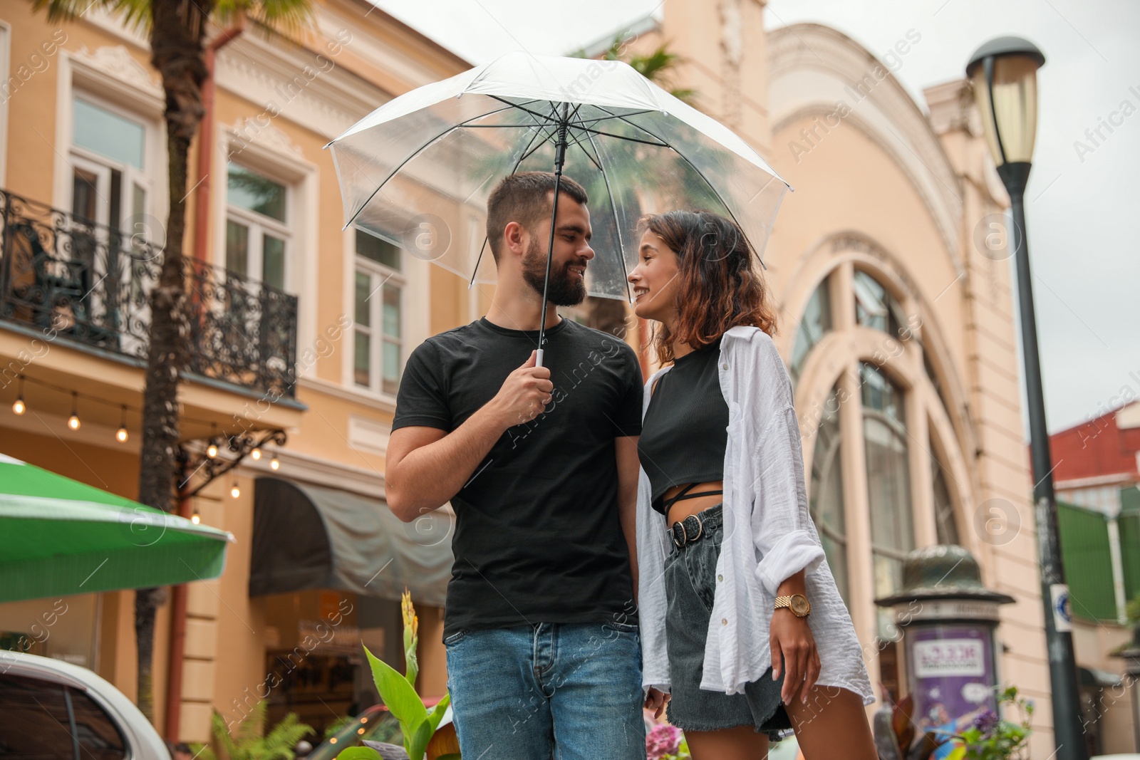 Photo of Young couple with umbrella enjoying time together under rain on city street