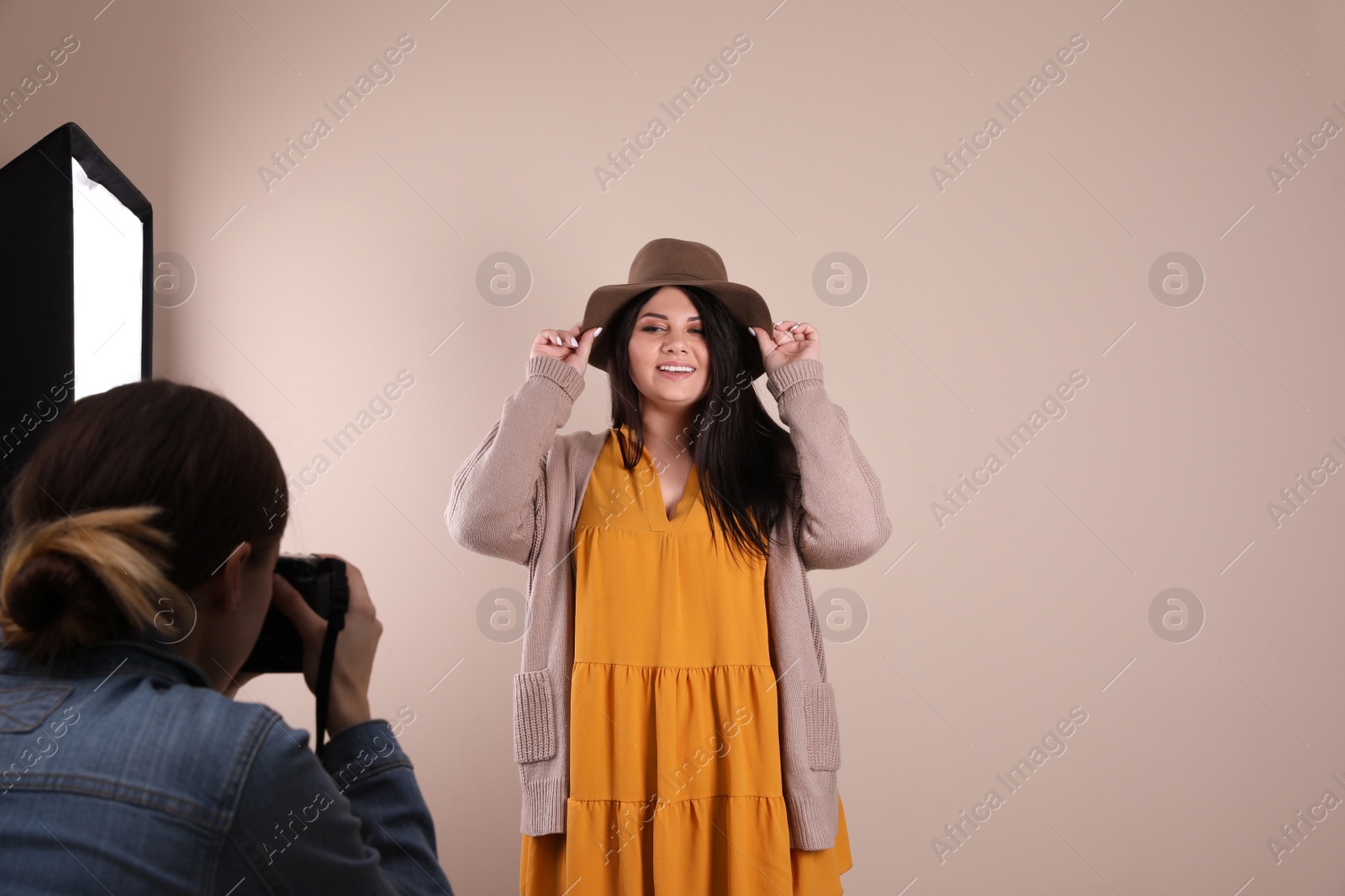 Photo of Photographer taking picture of overweight woman on beige background. Plus size model