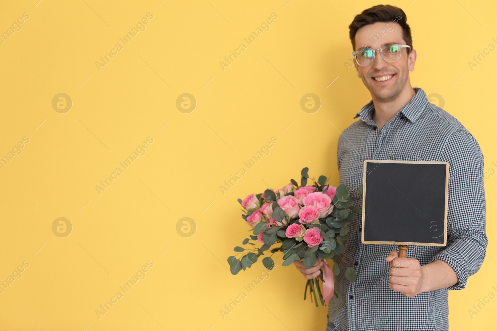 Photo of Male florist holding small chalkboard and bouquet on color background