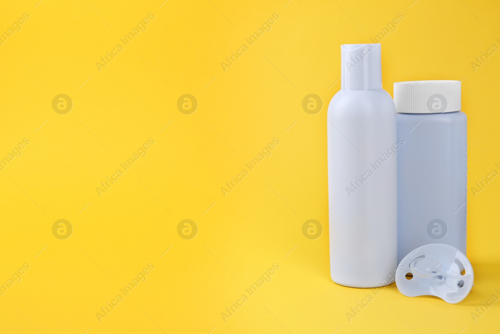 Photo of Bottles with baby powder, lotion and pacifier on yellow background. Space for text