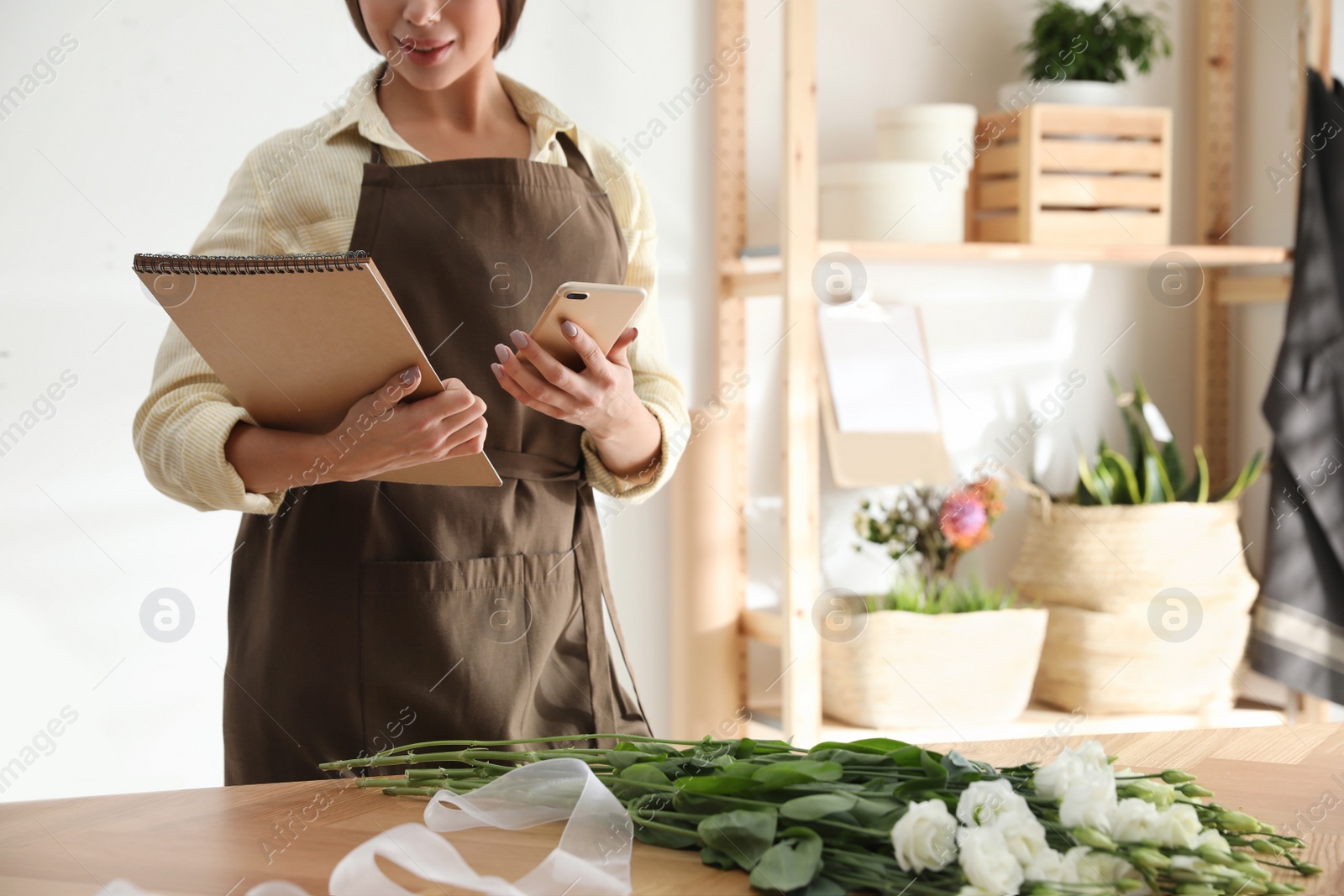 Photo of Florist with notebook and smartphone in workshop, closeup