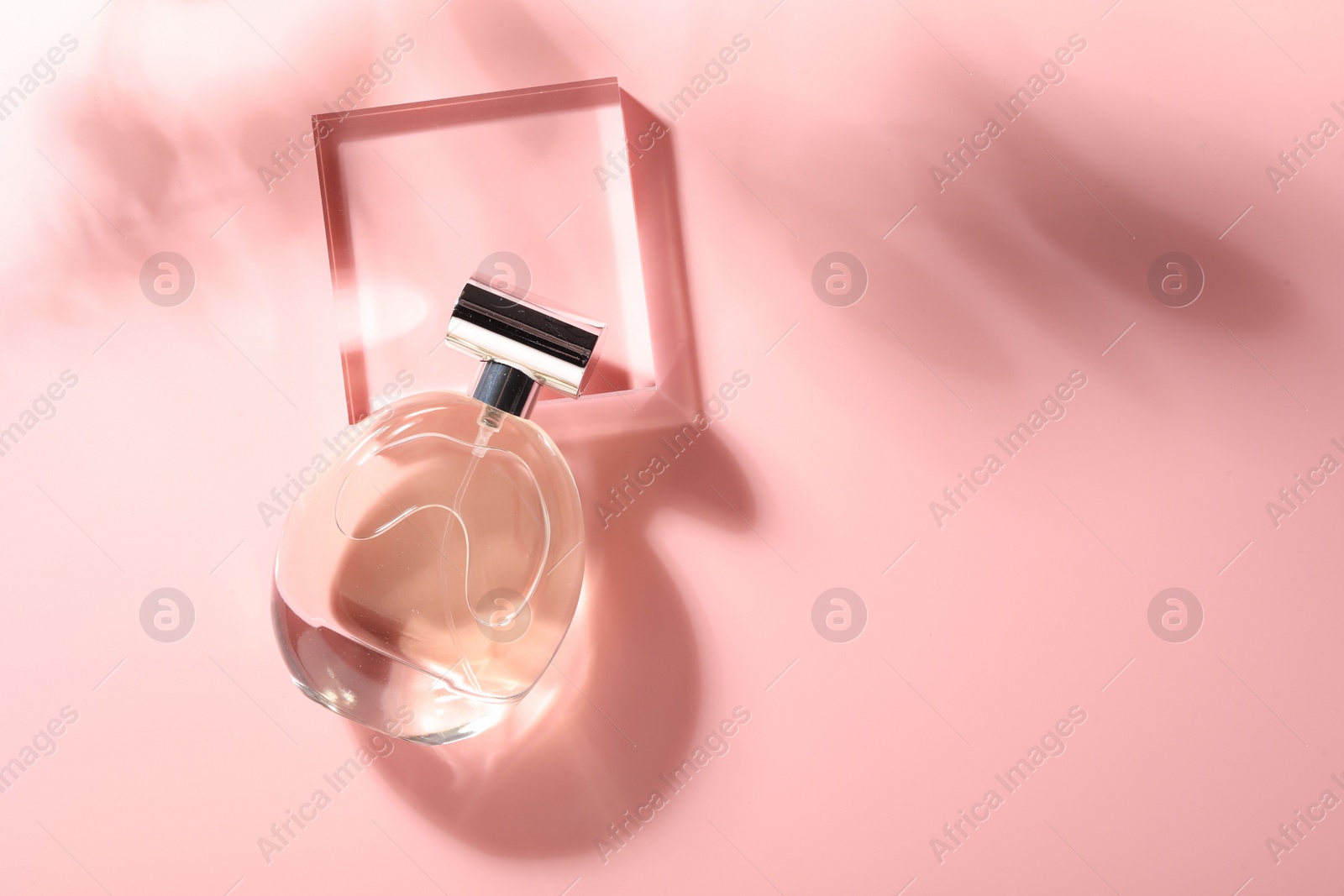 Photo of Bottle of luxury women's perfume in sunlight on pink background, top view. Space for text