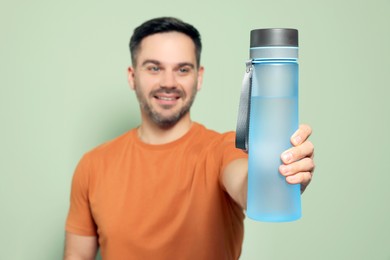 Happy man showing transparent plastic bottle of water against light green background, focus on hand