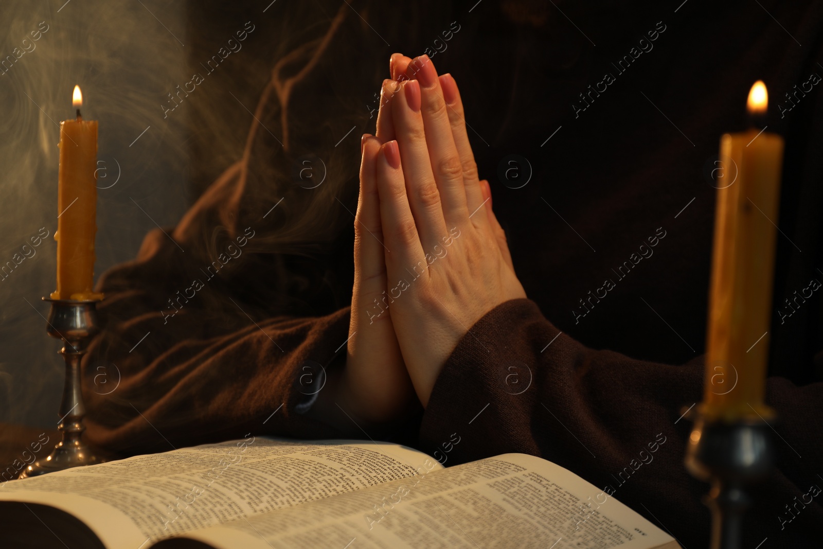 Photo of Woman praying at table with burning candles and Bible, closeup