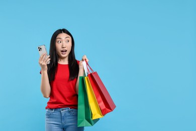 Photo of Surprised woman with shopping bags and smartphone on light blue background. Space for text