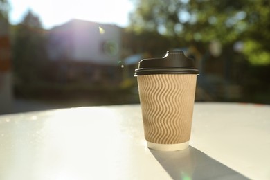 Cardboard takeaway coffee cup with plastic lid on white table outdoors, space for text