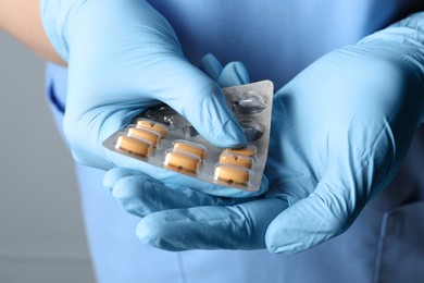 Doctor taking pill out from blister pack on grey background, closeup