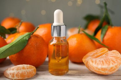 Bottle of tangerine essential oil and fresh fruits on white wooden table, closeup