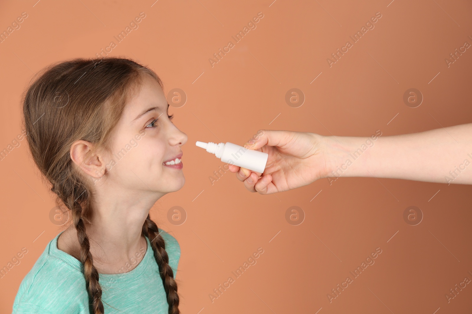 Photo of Mother helping her daughter to use nasal spray on coral background