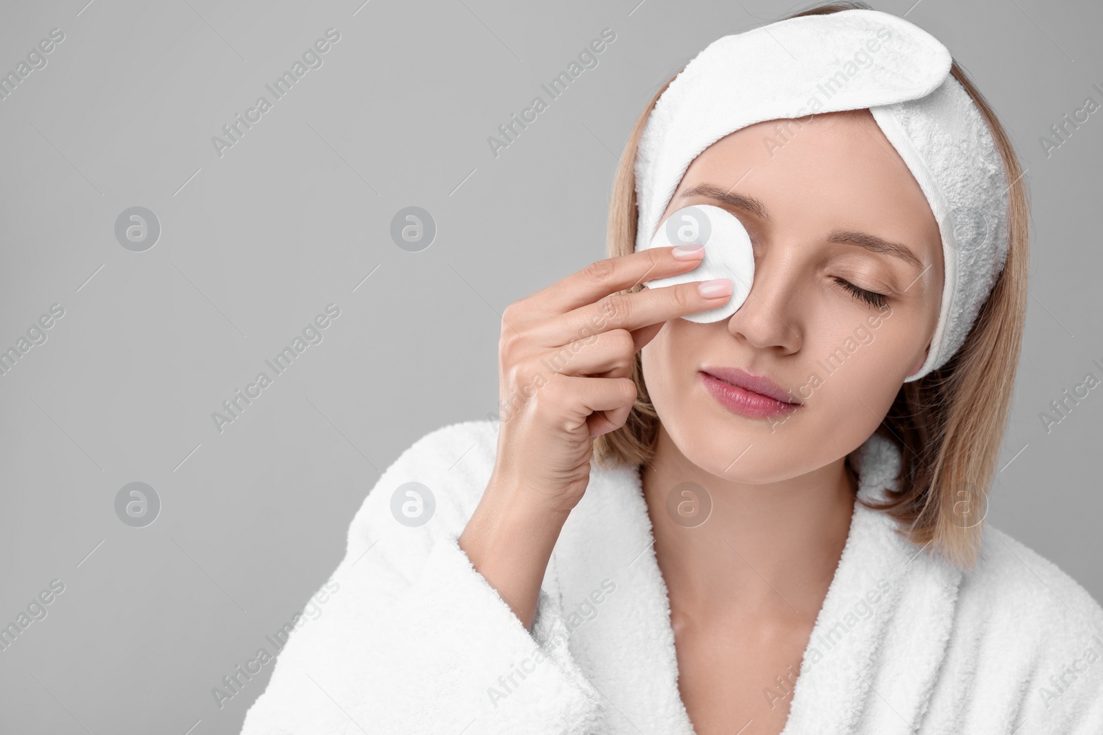 Photo of Young woman cleaning face with cotton pad on light grey background. Space for text