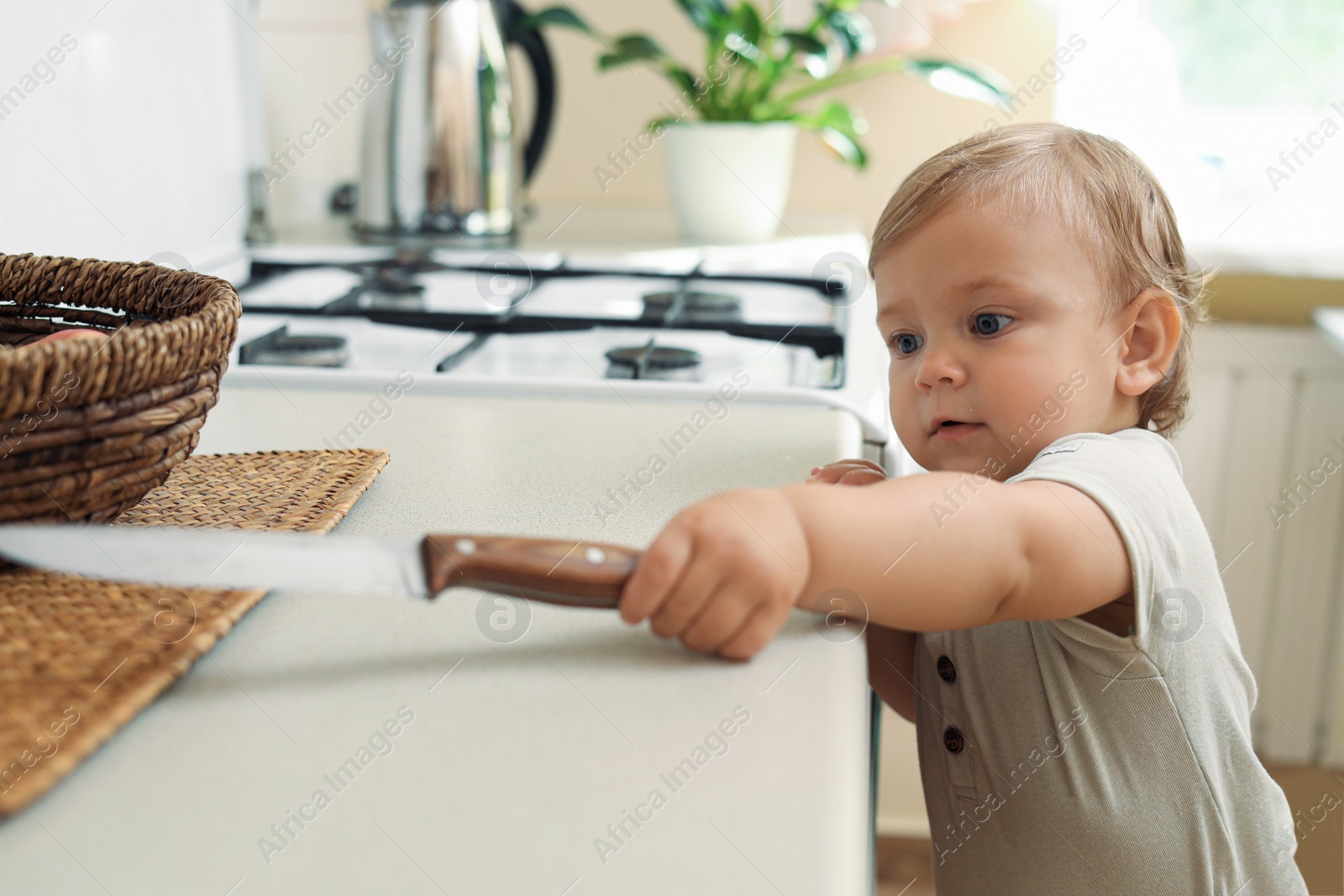 Photo of Little child holding sharp knife in kitchen. Dangerous situation