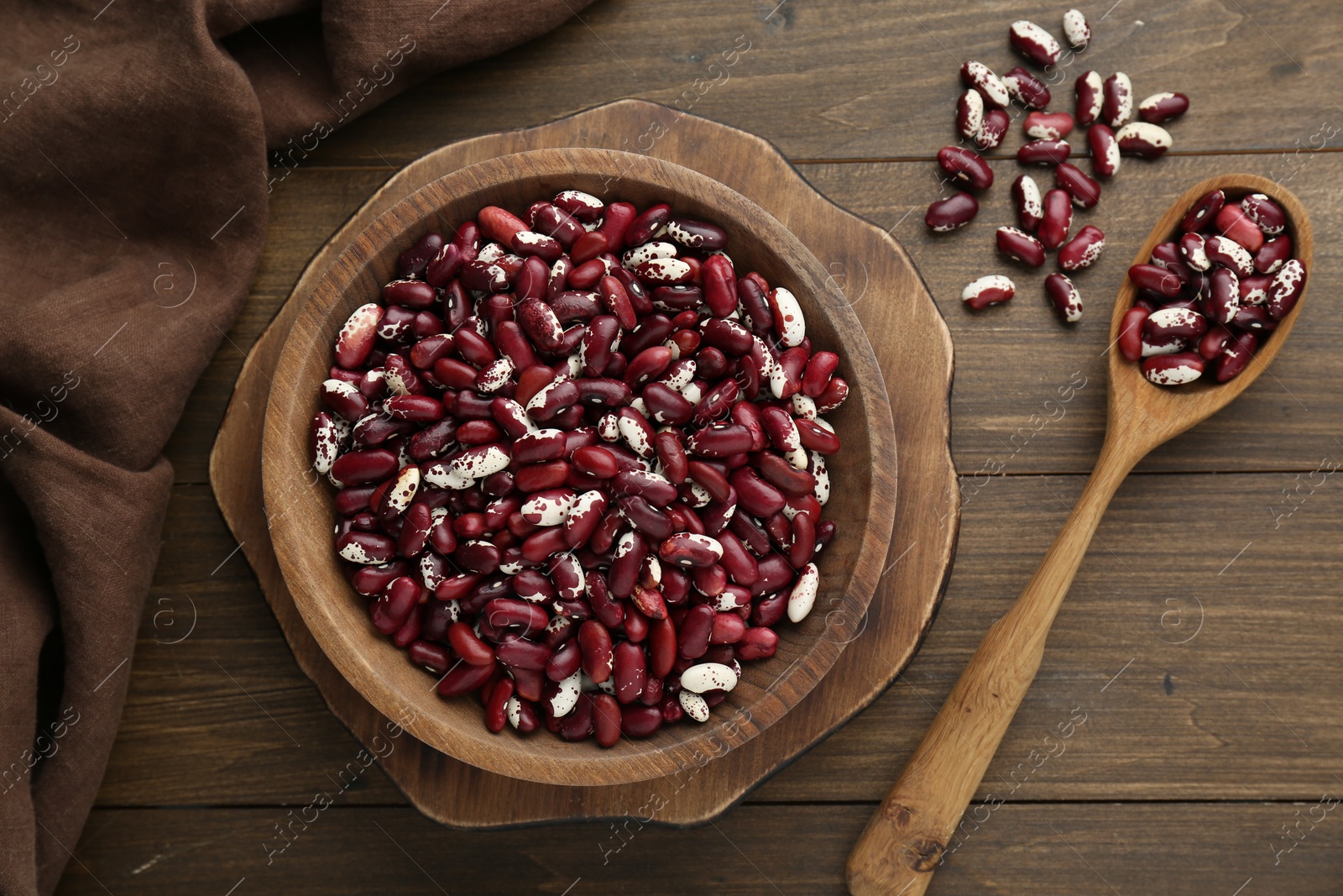 Photo of Bowl and spoon with dry kidney beans on wooden table, flat lay