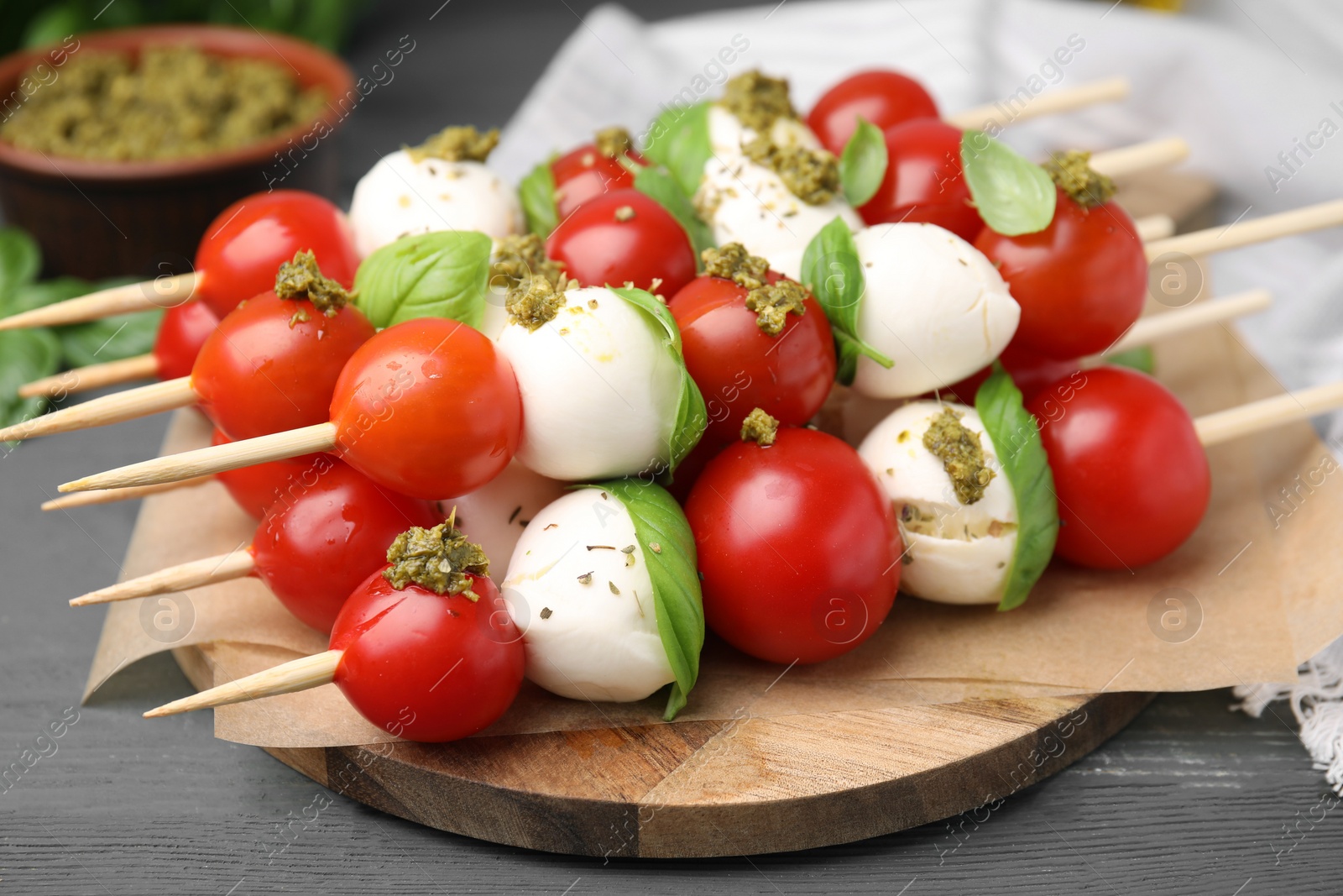 Photo of Caprese skewers with tomatoes, mozzarella balls, basil and pesto sauce on grey wooden table, closeup
