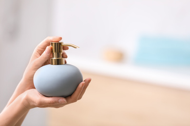 Photo of Woman holding soap dispenser on blurred background, closeup. Space for text