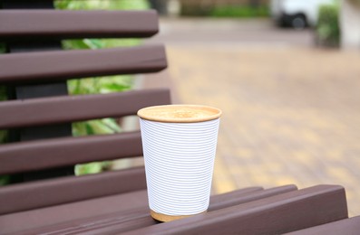 Photo of Paper cup of coffee on wooden bench outdoors. Takeaway drink