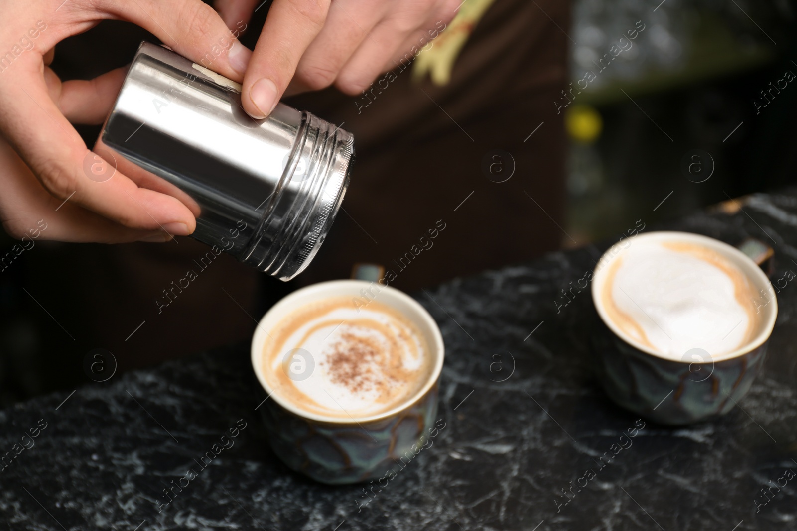 Photo of Barista decorating coffee with cinnamon at table, closeup