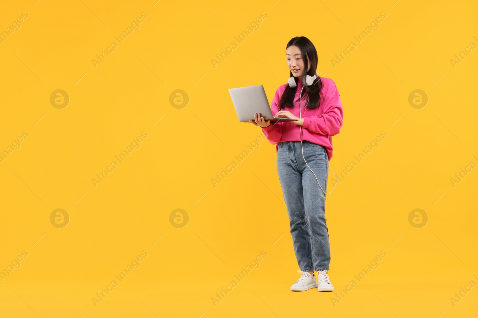 Photo of Portrait of smiling woman with headphones and laptop on orange background. Space for text