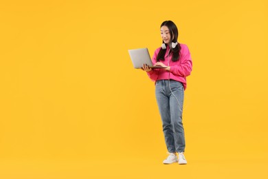 Portrait of smiling woman with headphones and laptop on orange background. Space for text