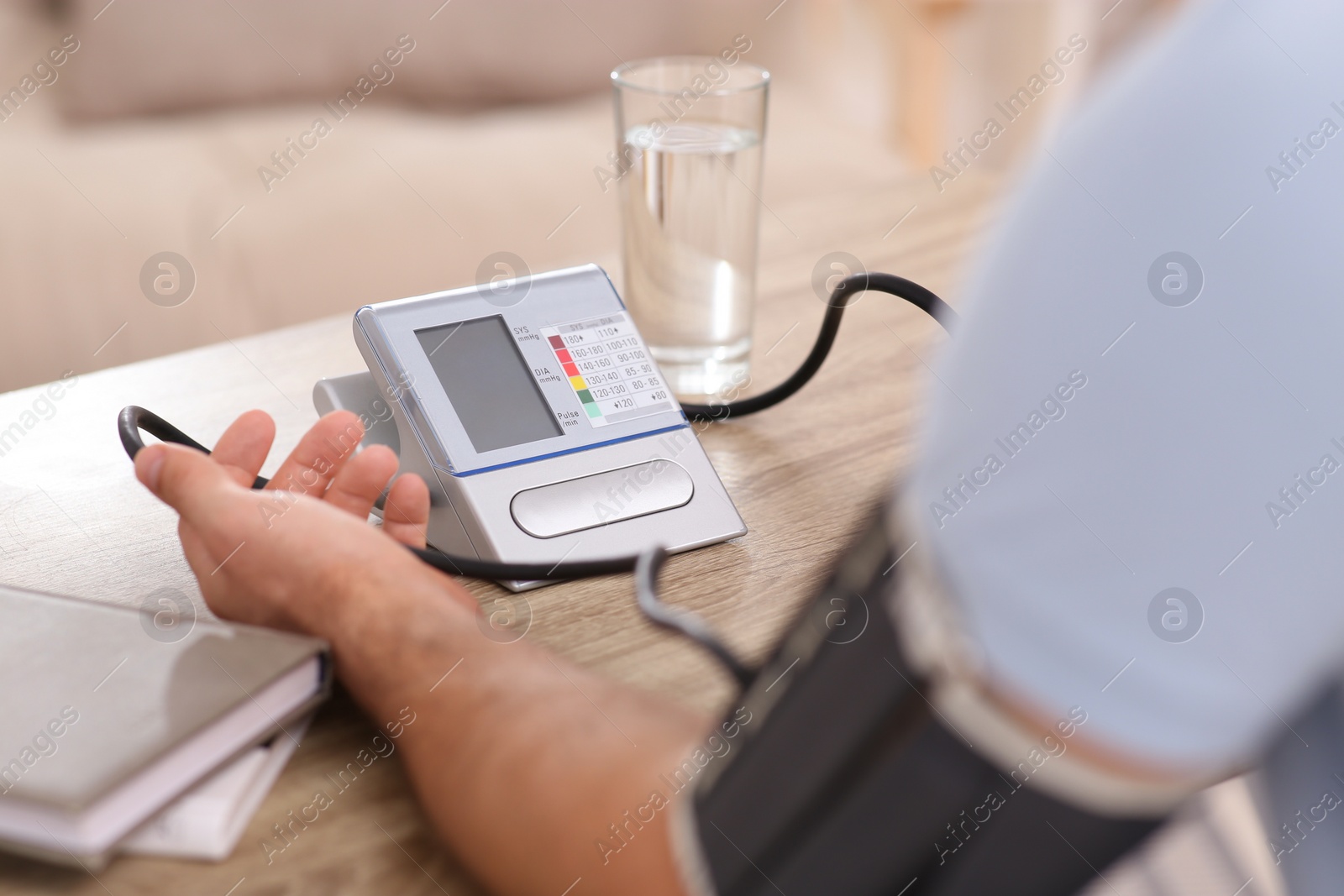 Photo of Man checking blood pressure at wooden table indoors, closeup