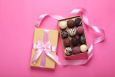 Photo of Open box with delicious chocolate candies and ribbon on pink background, top view