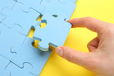 Woman putting light blue puzzle piece on yellow background, closeup. Career promotion concept