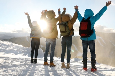 Group of excited friends with backpacks enjoying mountain view during winter vacation