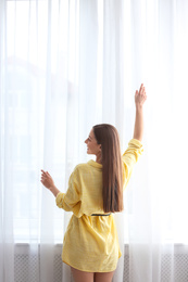 Photo of Young woman near window with curtains indoors