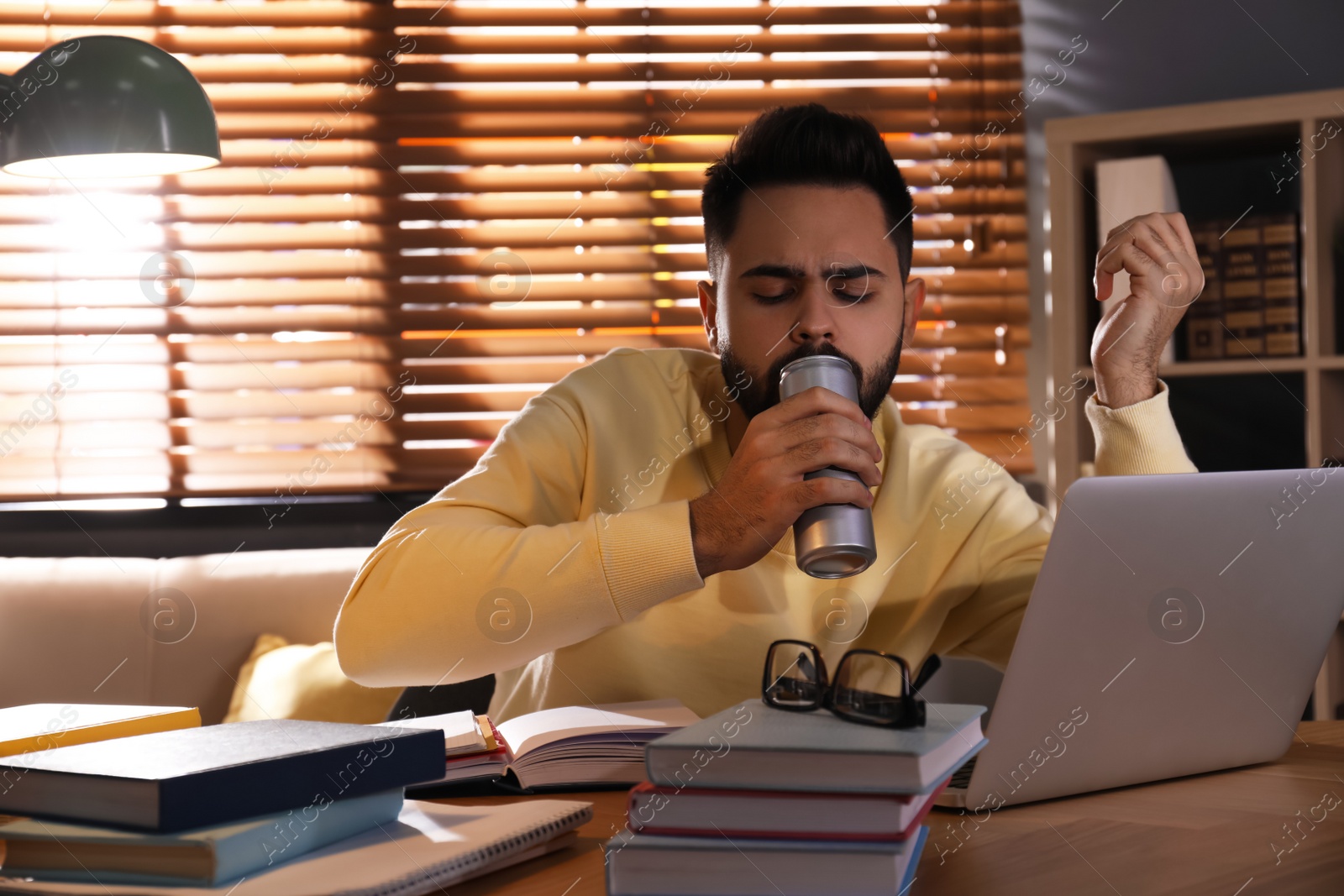 Photo of Tired young man with energy drink studying at home