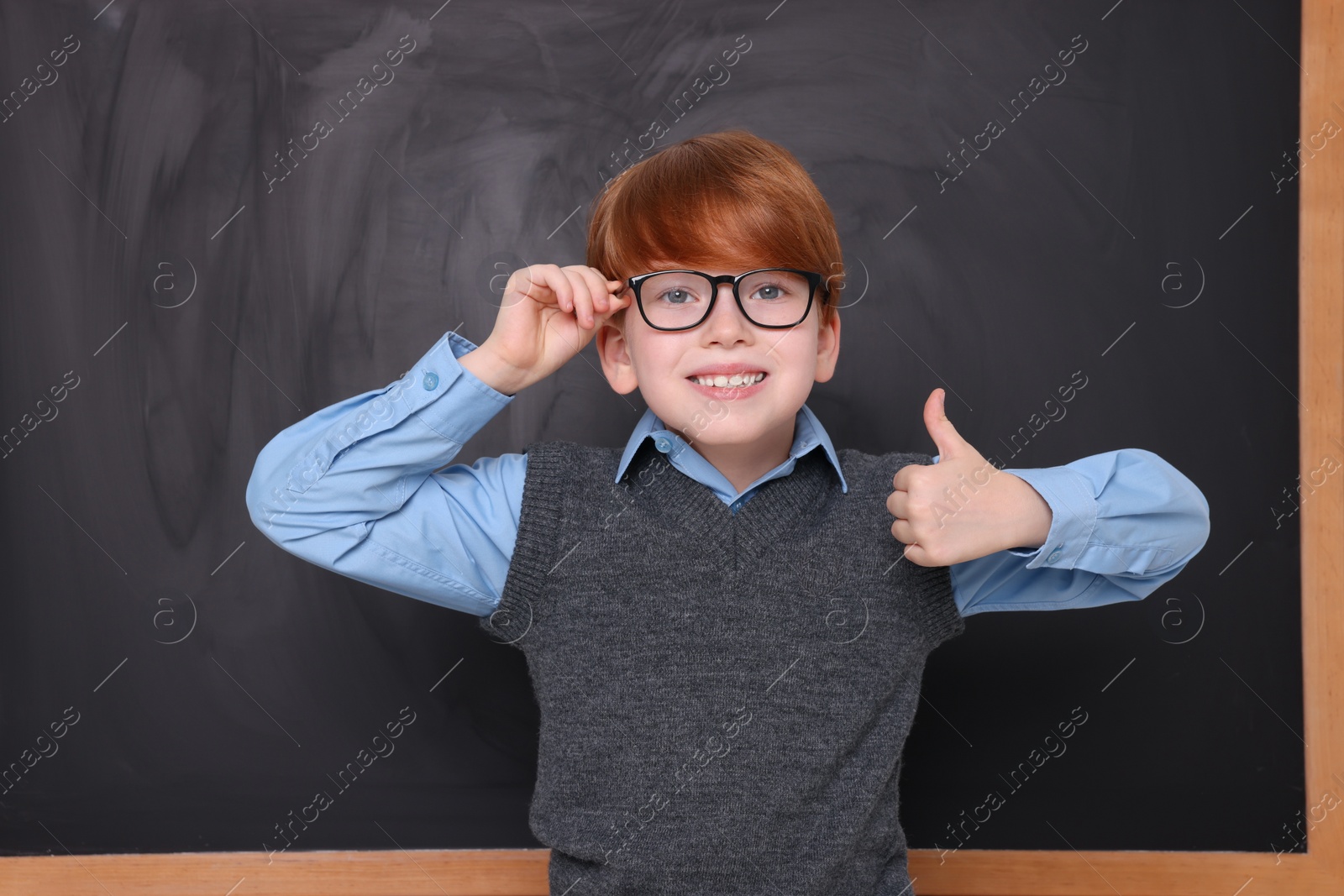 Photo of Smiling schoolboy showing thumb up near blackboard