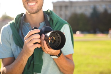 Young male photographer holding professional camera on street. Space for text