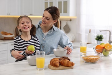 Photo of Mother and her cute little daughter having breakfast at table in kitchen