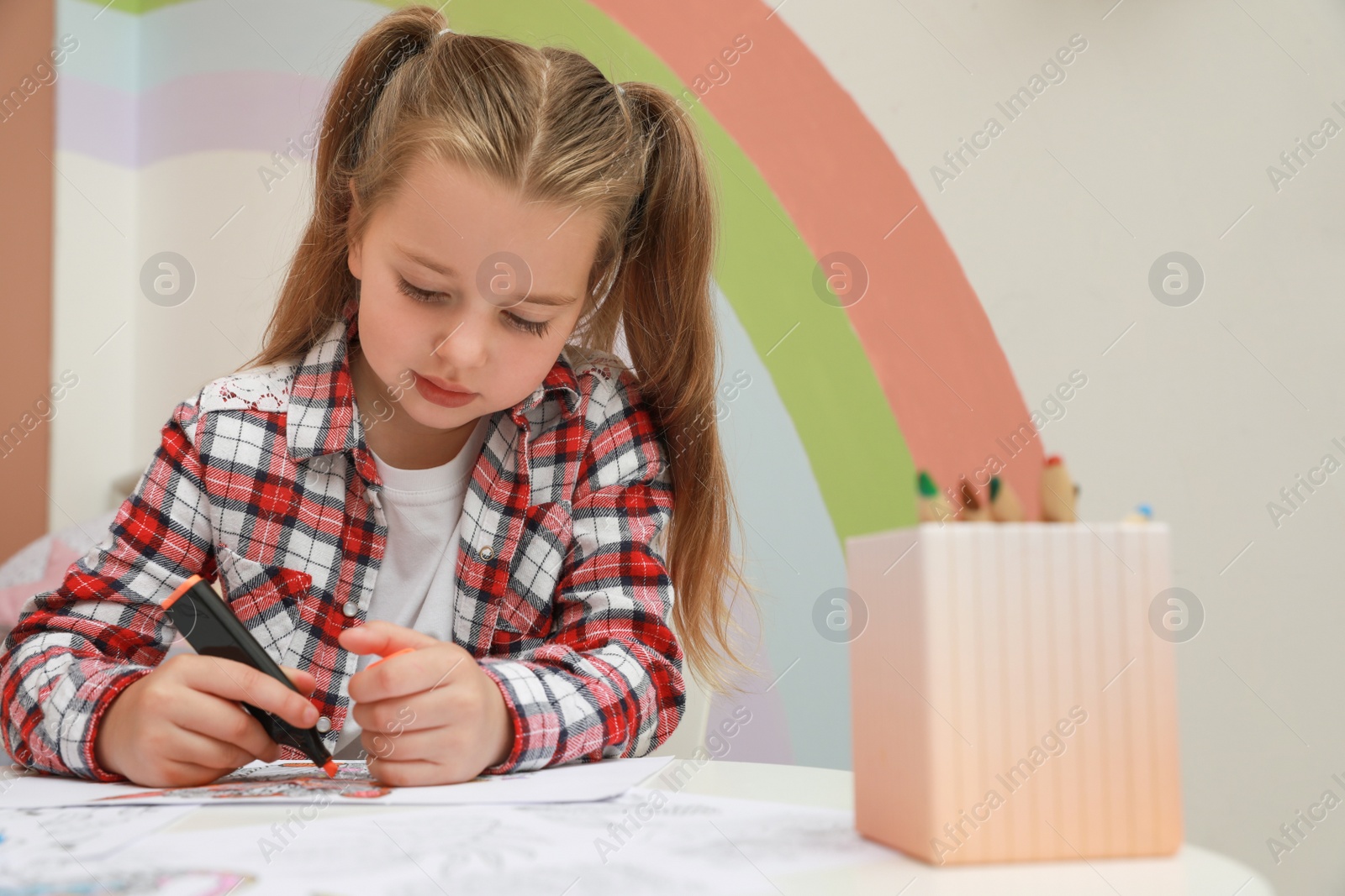 Photo of Little girl coloring antistress page at table indoors