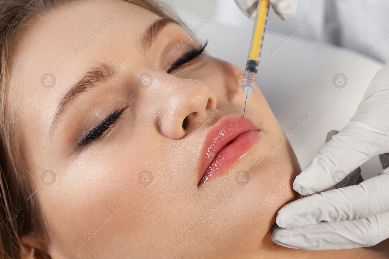 Photo of Young woman getting lips injection in clinic, closeup. Cosmetic surgery