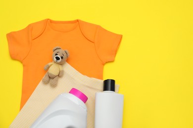 Bottles of laundry detergents, baby clothes and toy bear on yellow background, flat lay. Space for text