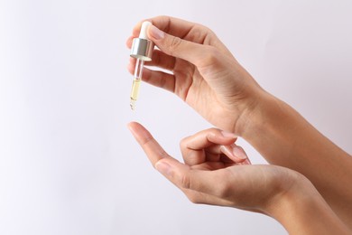 Woman applying cosmetic serum onto her finger on white background, closeup