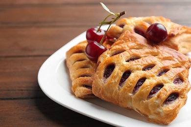 Photo of Fresh delicious puff pastry with sweet cherries served on wooden table, closeup