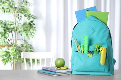 Stylish backpack with different school stationery on table indoors. Space for text