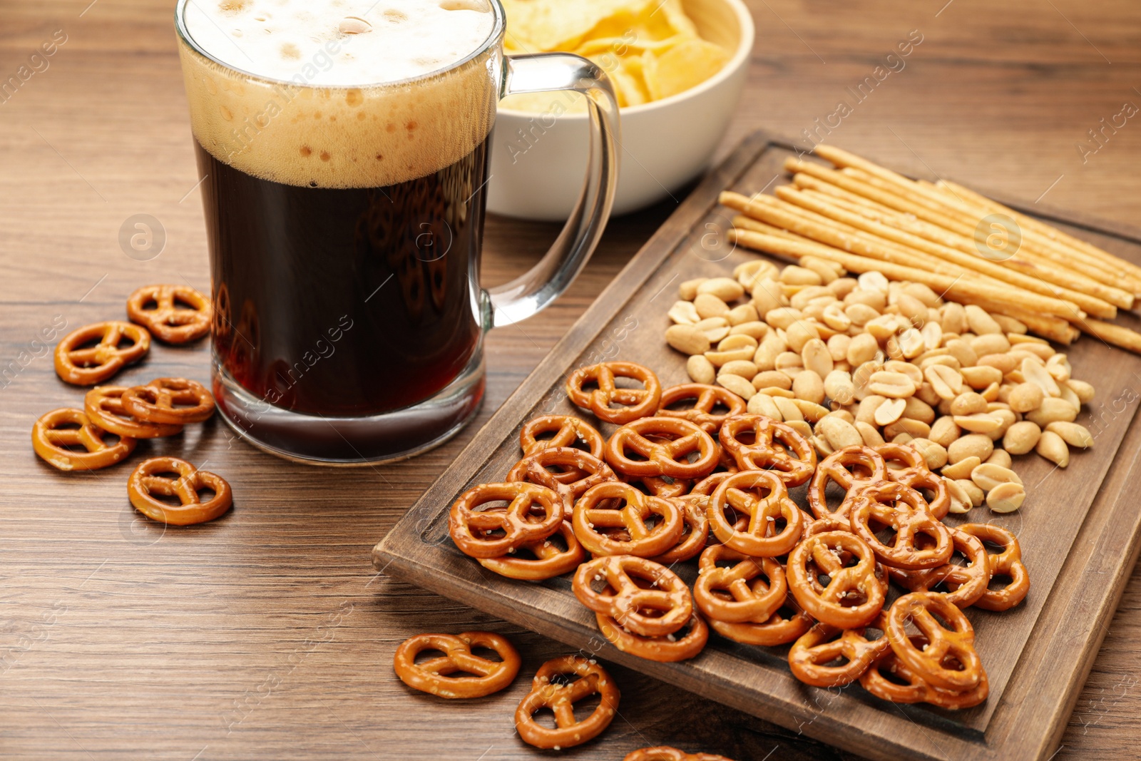 Photo of Glass of beer served with delicious pretzel crackers and other snacks on wooden table