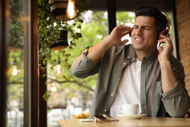 Photo of Handsome man with headphones listening to music in cafe