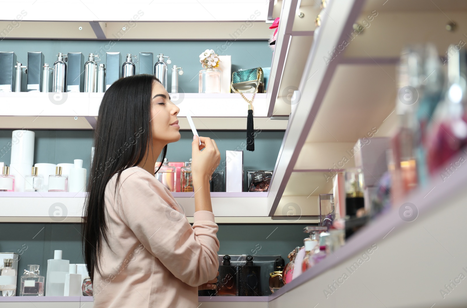 Image of Beautiful young woman choosing perfume in shop