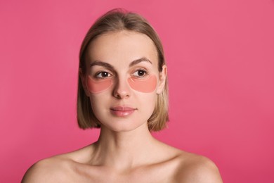 Beautiful young woman with under eye patches on pink background