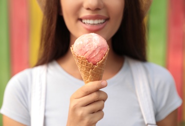 Happy young woman with delicious ice cream in waffle cone outdoors, closeup