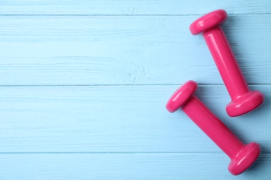 Bright dumbbells and space for text on wooden background, flat lay. Home fitness