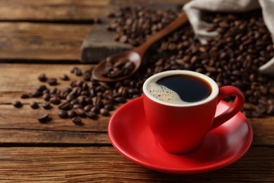 Photo of Cup of aromatic coffee and beans on wooden table. Space for text