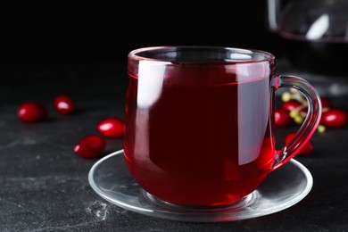Photo of Glass cup of fresh dogwood tea and berries on black table, closeup