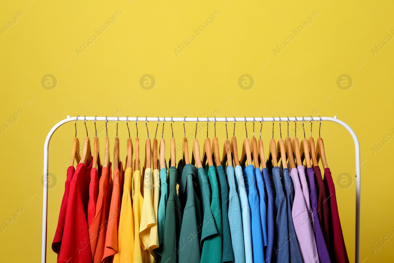 Photo of Rack with bright clothes on yellow background. Rainbow colors